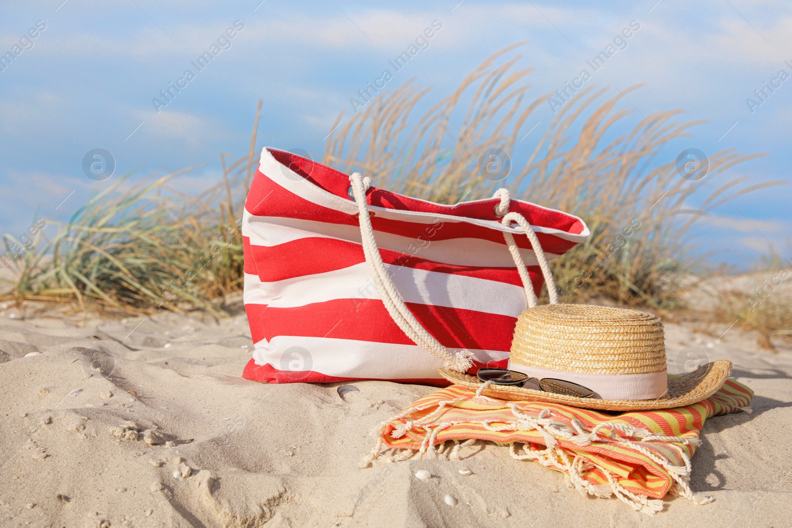 Photo of Beach bag, towel, straw hat and sunglasses on sand