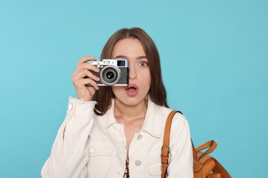 Emotional young woman with camera taking photo on light blue background. Interesting hobby