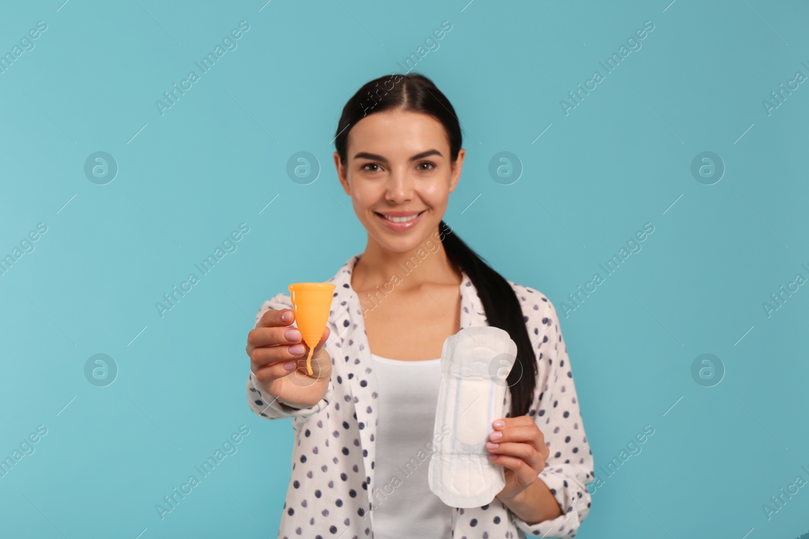 Photo of Young woman with menstrual cup and pad on light blue background