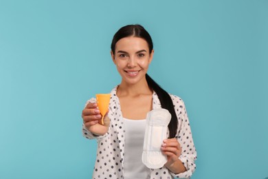 Photo of Young woman with menstrual cup and pad on light blue background