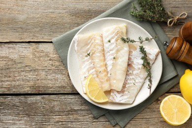 Photo of Fresh raw cod fillets with thyme and lemon on wooden table, flat lay. Space for text