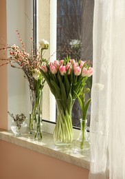 Photo of Many different spring flowers and branches with leaves on windowsill indoors