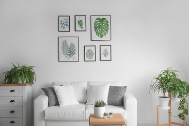 Photo of Beautiful paintings of tropical leaves over sofa in living room interior