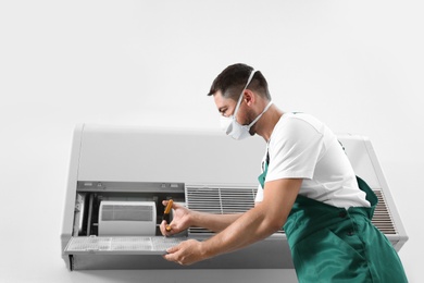 Professional male technician repairing air conditioner indoors