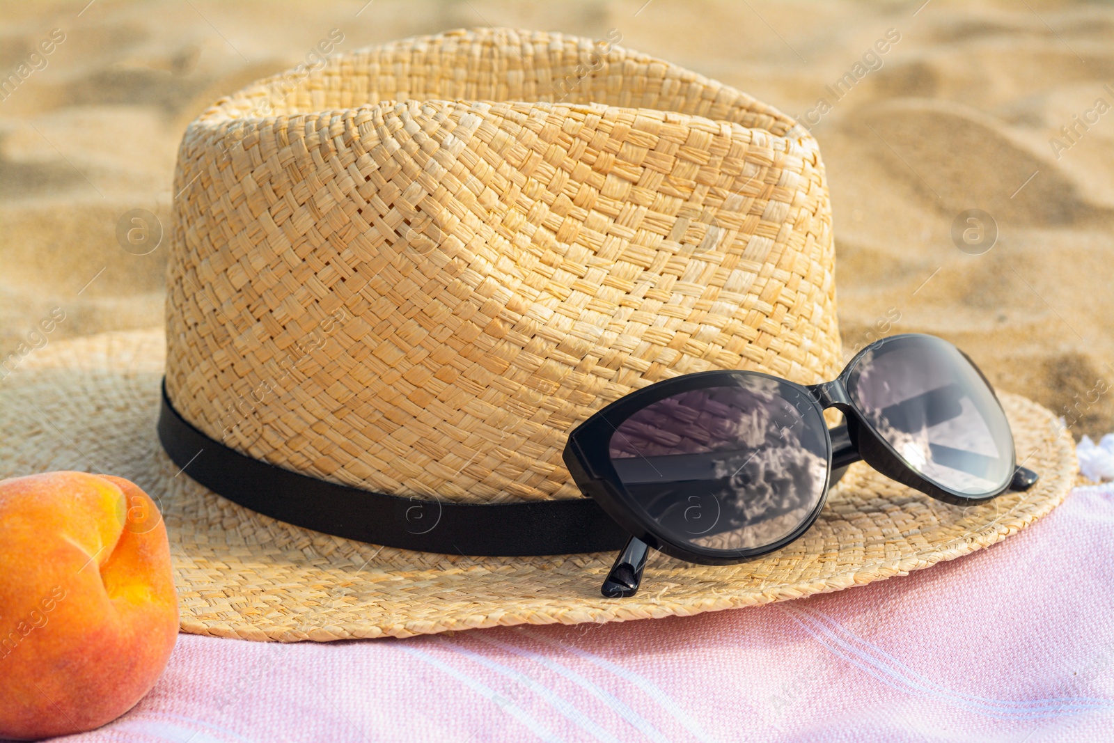 Photo of Hat with beautiful sunglasses and peach on sand, closeup