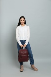 Young woman with stylish backpack on light grey background