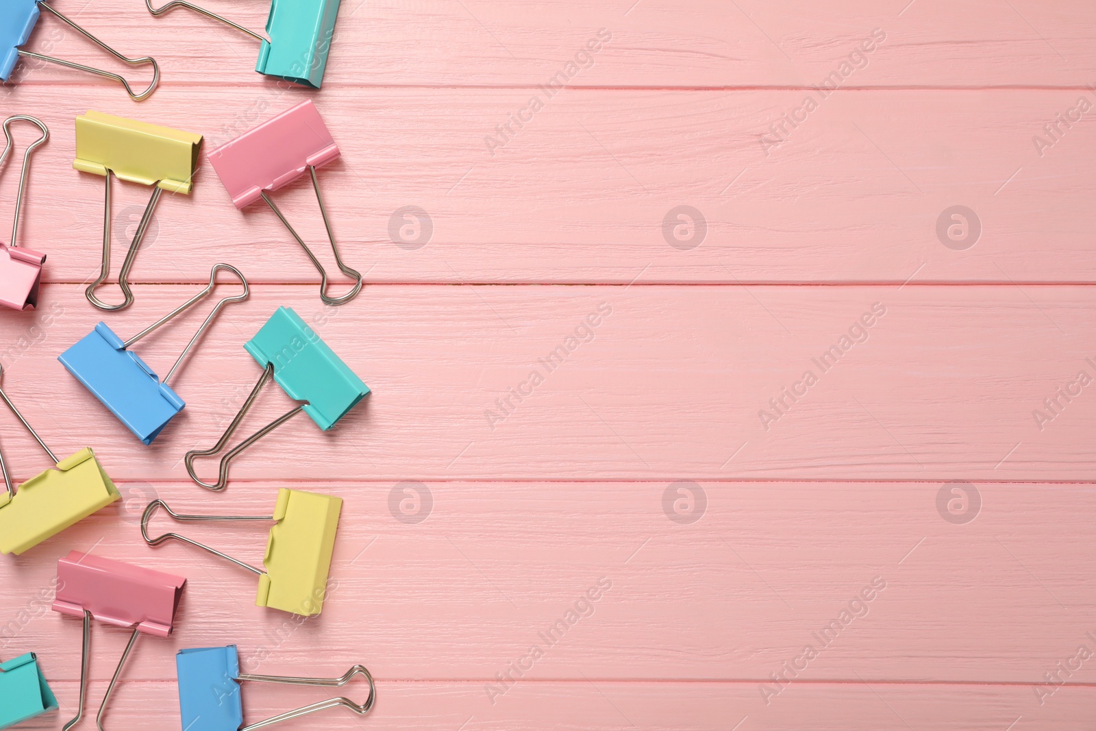 Photo of Colorful binder clips on pink wooden background, flat lay. Space for text