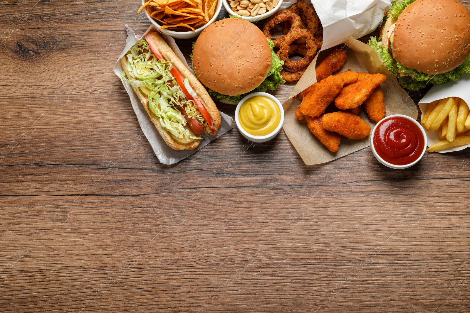 Photo of French fries, burgers and other fast food on wooden table, flat lay with space for text