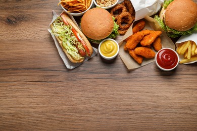 Photo of French fries, burgers and other fast food on wooden table, flat lay with space for text