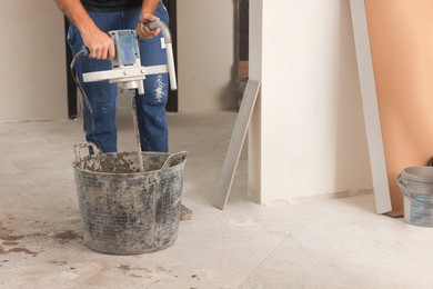 Photo of Professional worker mixing cement in bucket indoors, closeup. Tiles installation process