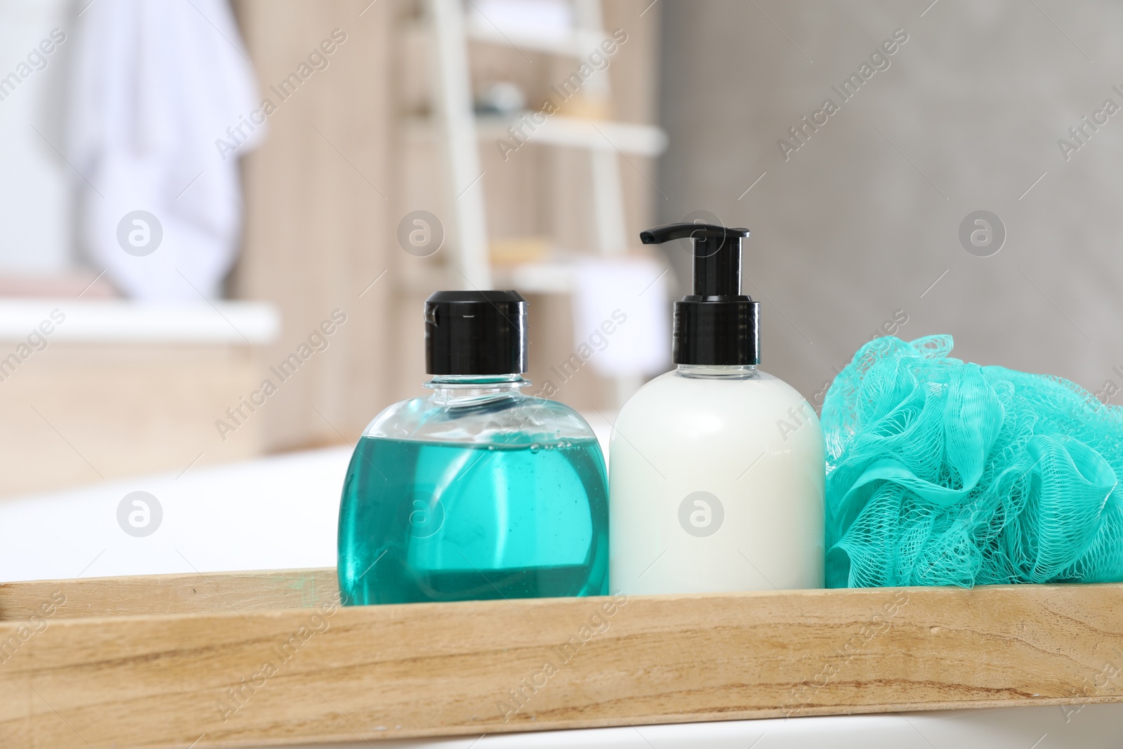 Photo of Wooden bath tray with bottles of shower gels and mesh pouf on tub indoors, closeup