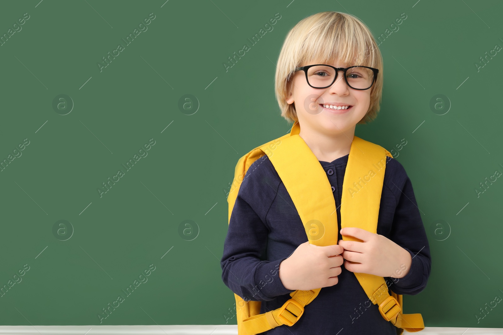 Photo of Happy little school child with backpack near chalkboard. Space for text