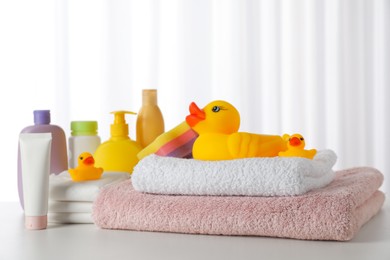 Photo of Towels, rubber ducks and baby care products on white table indoors