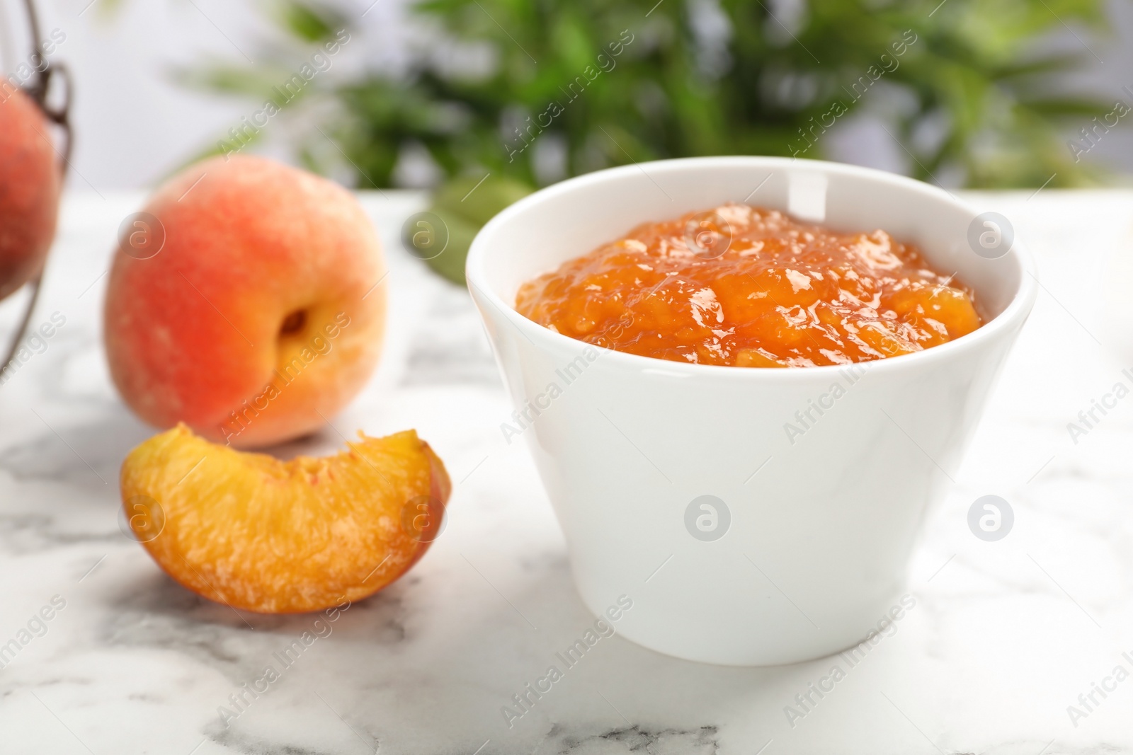 Photo of Bowl with tasty peach jam on marble table