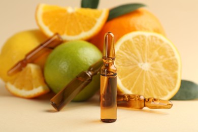 Skincare ampoules with vitamin C, different citrus fruits and leaves on beige background, closeup