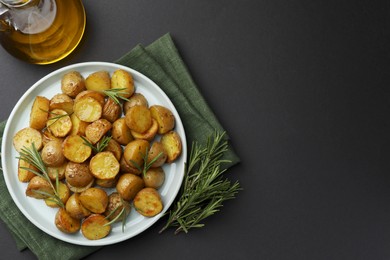 Delicious baked potatoes with rosemary and oil on black table, top view. Space for text