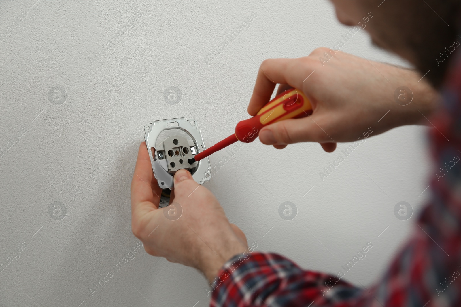 Photo of Electrician with screwdriver repairing power socket, closeup