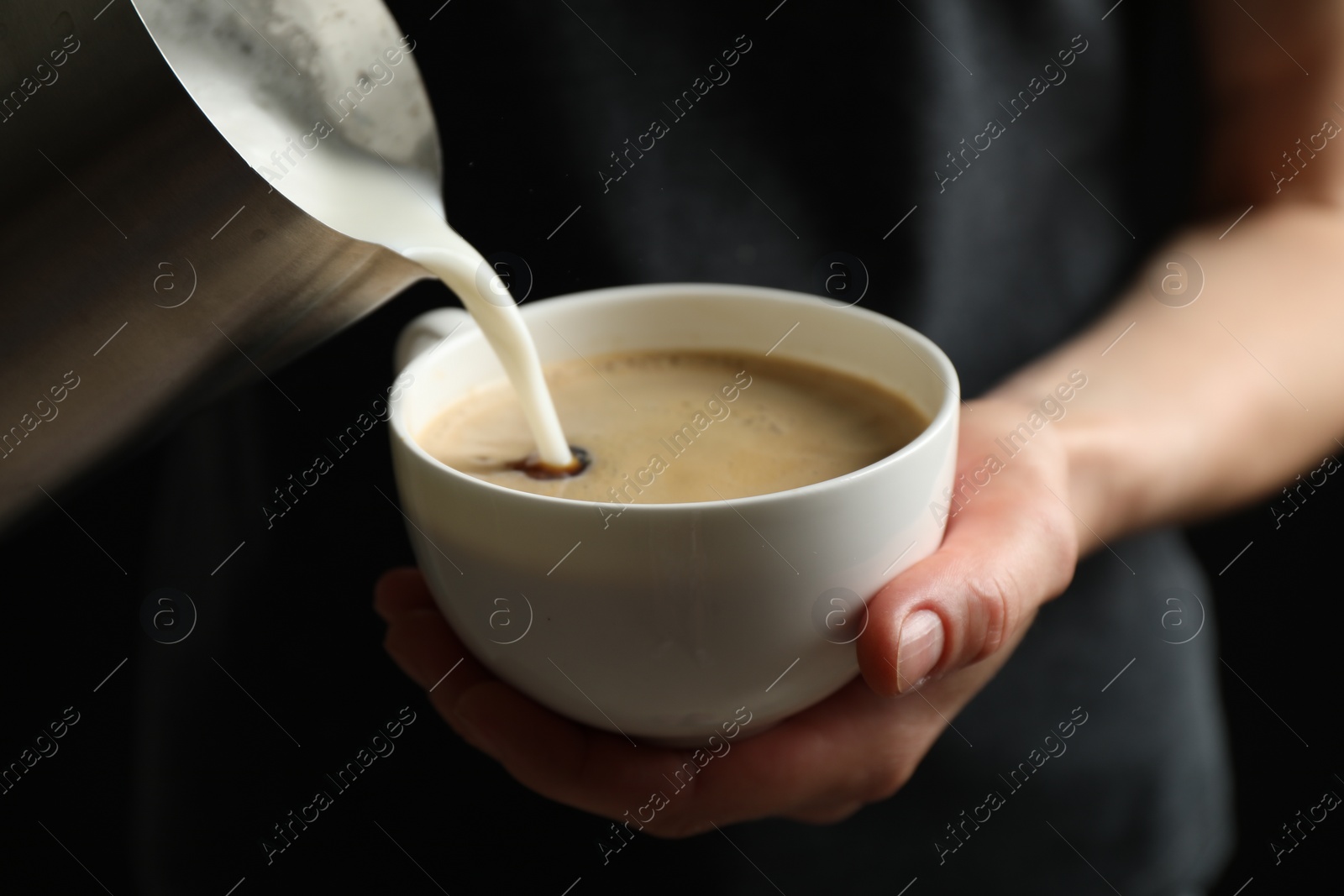 Photo of Woman pouring milk into cup of hot coffee, closeup