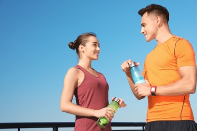 Photo of Young sporty couple with bottles of water outdoors on sunny day. Space for text