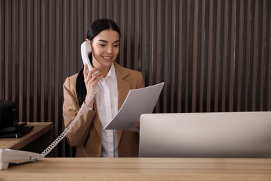 Photo of Receptionist with papers talking on phone at countertop in office