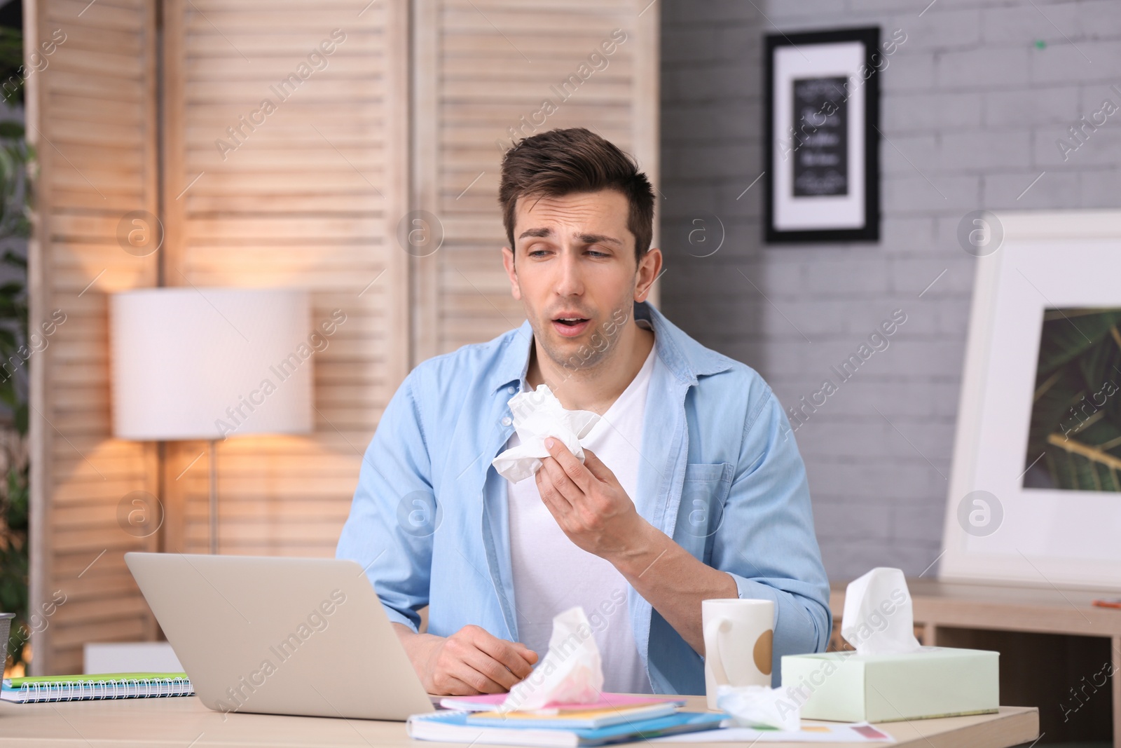 Photo of Sad exhausted man with tissue suffering from cold while working with laptop at table