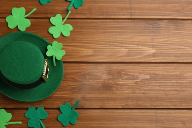 Leprechaun hat and decorative clover leaves on wooden table, flat lay with space for text. St Patrick's Day celebration