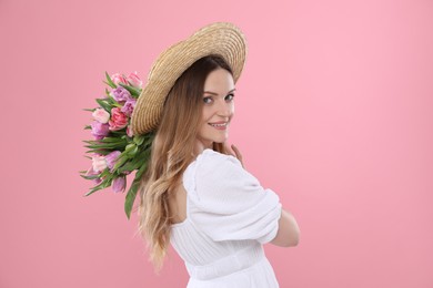 Happy young woman in straw hat holding bouquet of beautiful tulips on pink background