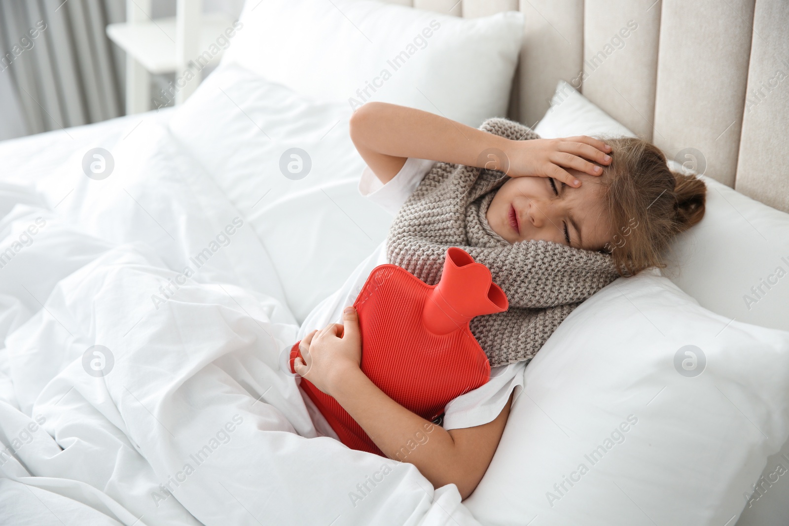 Photo of Ill girl with hot water bottle suffering from cold in bed at home