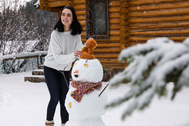 Young woman near funny snowman outdoors. Winter vacation
