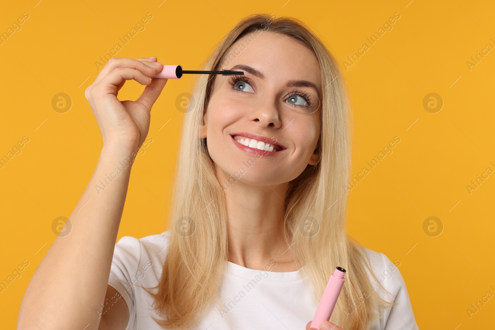 Photo of Beautiful woman applying mascara on orange background