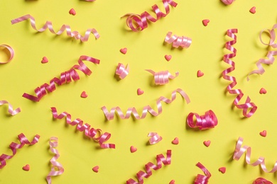 Photo of Serpentine streamers and heart shaped confetti on yellow background, flat lay