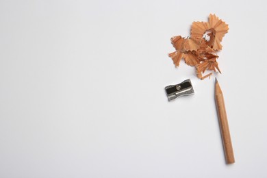 Sharp graphite pencil, shavings and sharpener on white background, flat lay. Space for text