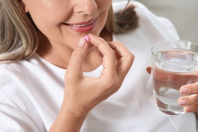 Photo of Senior woman with glass of water taking pill on blurred background, closeup