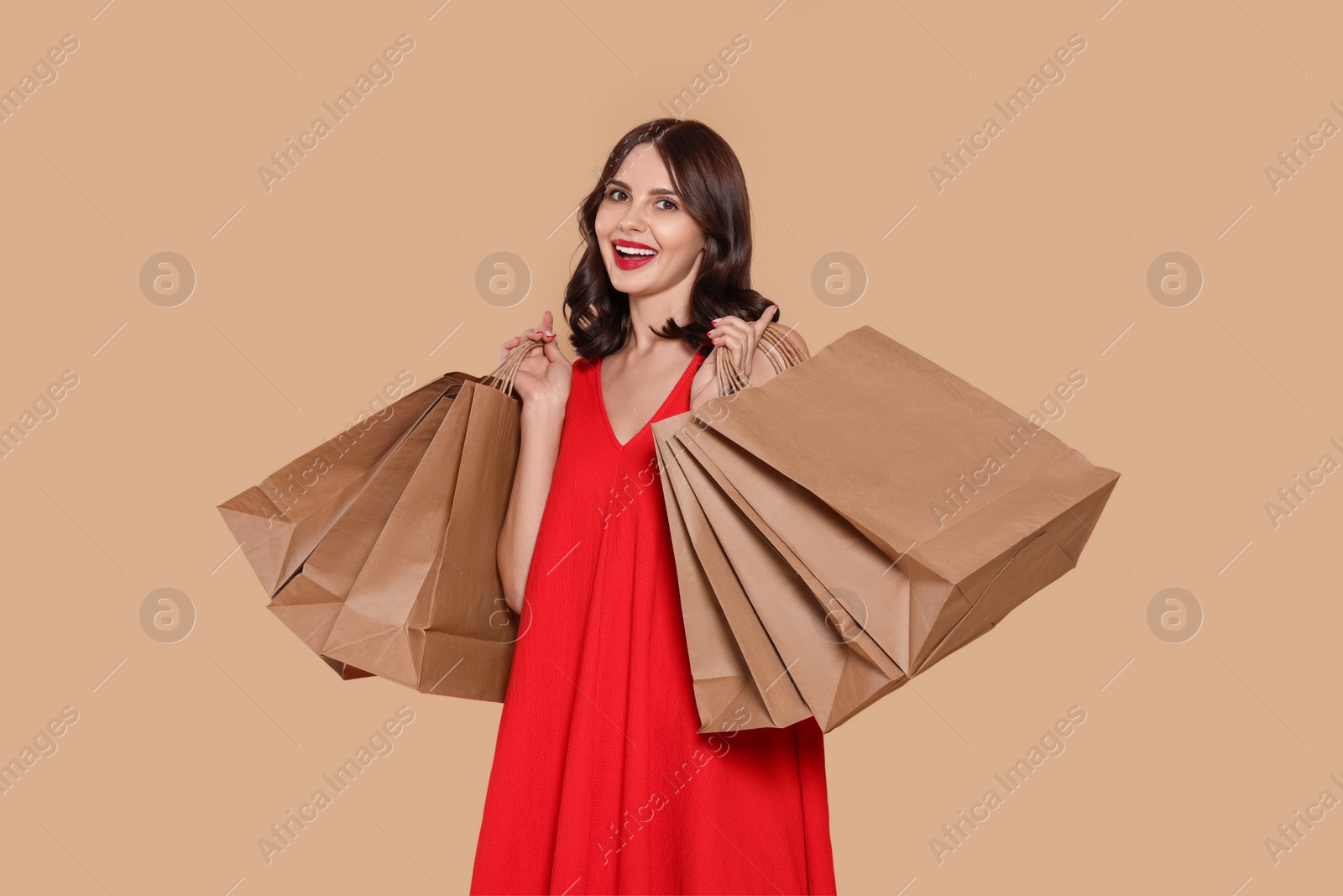 Photo of Beautiful young woman with paper shopping bags on beige background