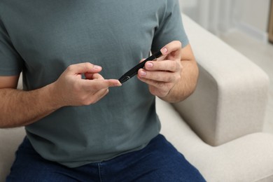 Diabetes test. Man checking blood sugar level with lancet pen at home, closeup