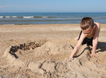 Little boy playing with sand near sea on sunny day