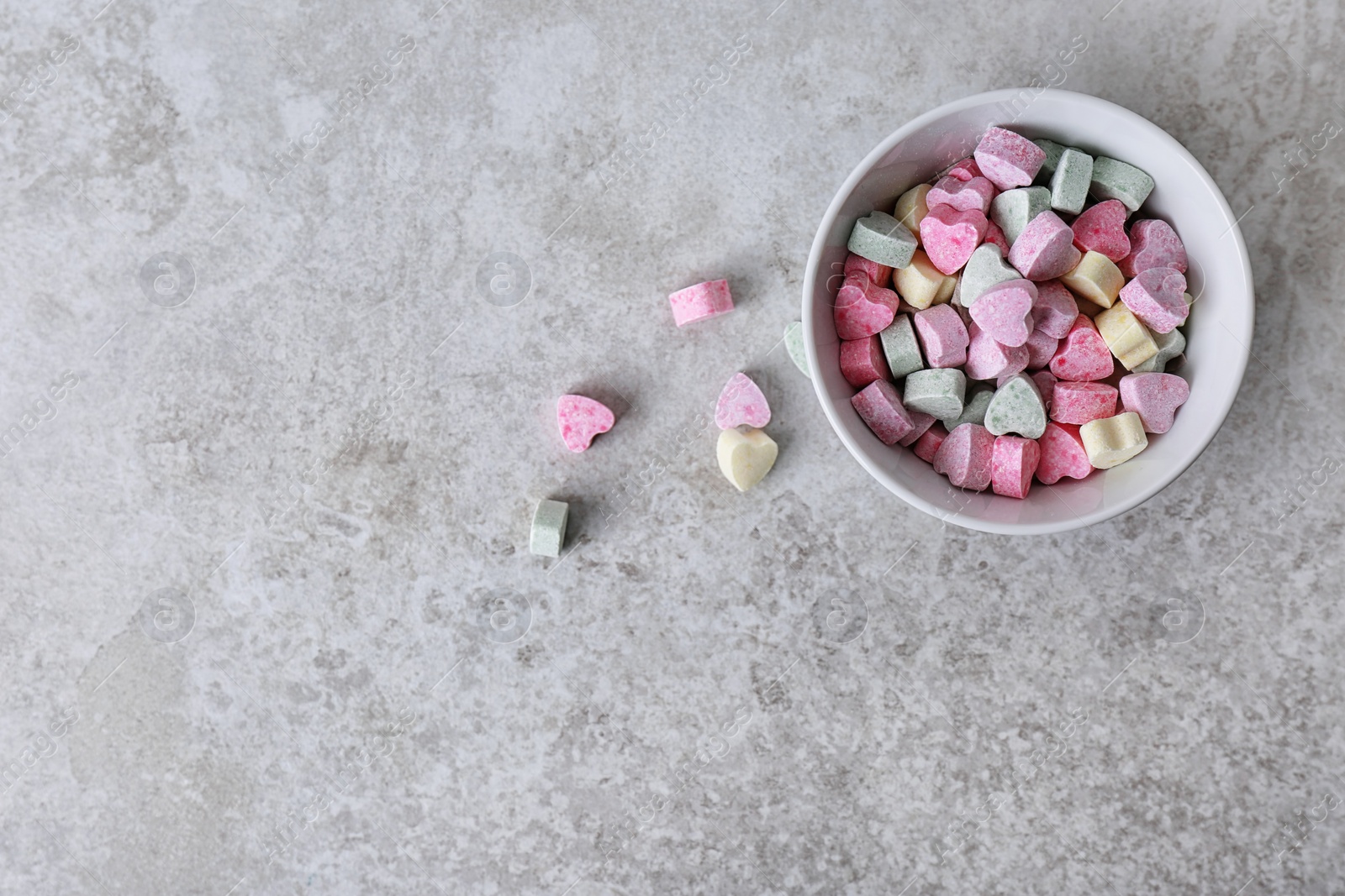 Photo of Small heart shaped candies and bowl on gray background, top view with space for text