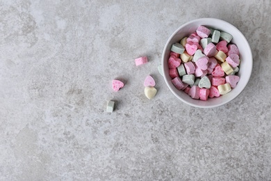 Small heart shaped candies and bowl on gray background, top view with space for text