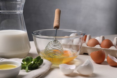 Photo of Metal whisk, raw eggs in bowl and ingredients on light table