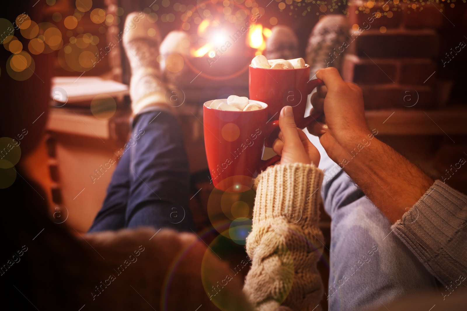 Image of Couple with cups of delicious cocoa resting near fireplace at home, closeup. Winter vacation