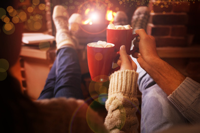 Image of Couple with cups of delicious cocoa resting near fireplace at home, closeup. Winter vacation