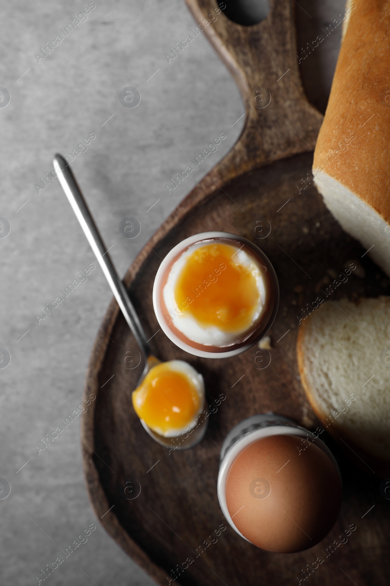 Photo of Fresh soft boiled eggs in cups and bread on grey table, flat lay