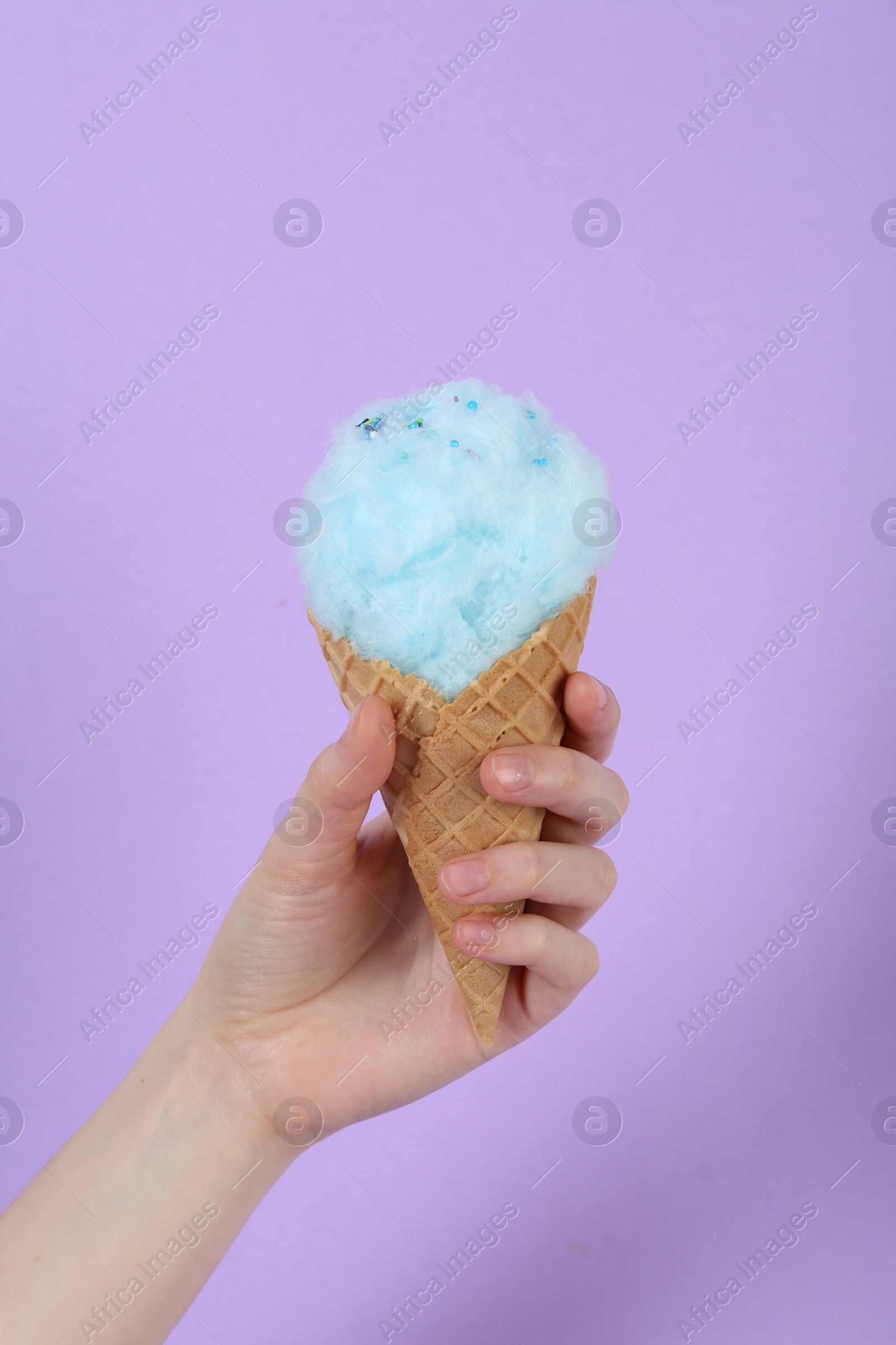 Photo of Woman holding waffle cone with cotton candy on violet background, closeup