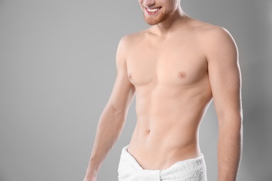 Young man with slim body in towel on grey background, closeup. Space for text