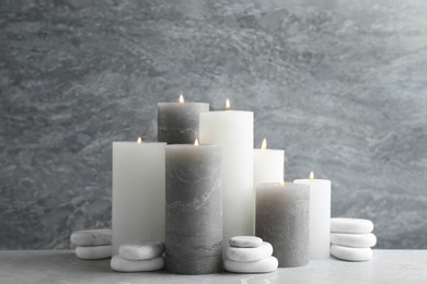 Set of burning candles with spa stones on table against grey marble background