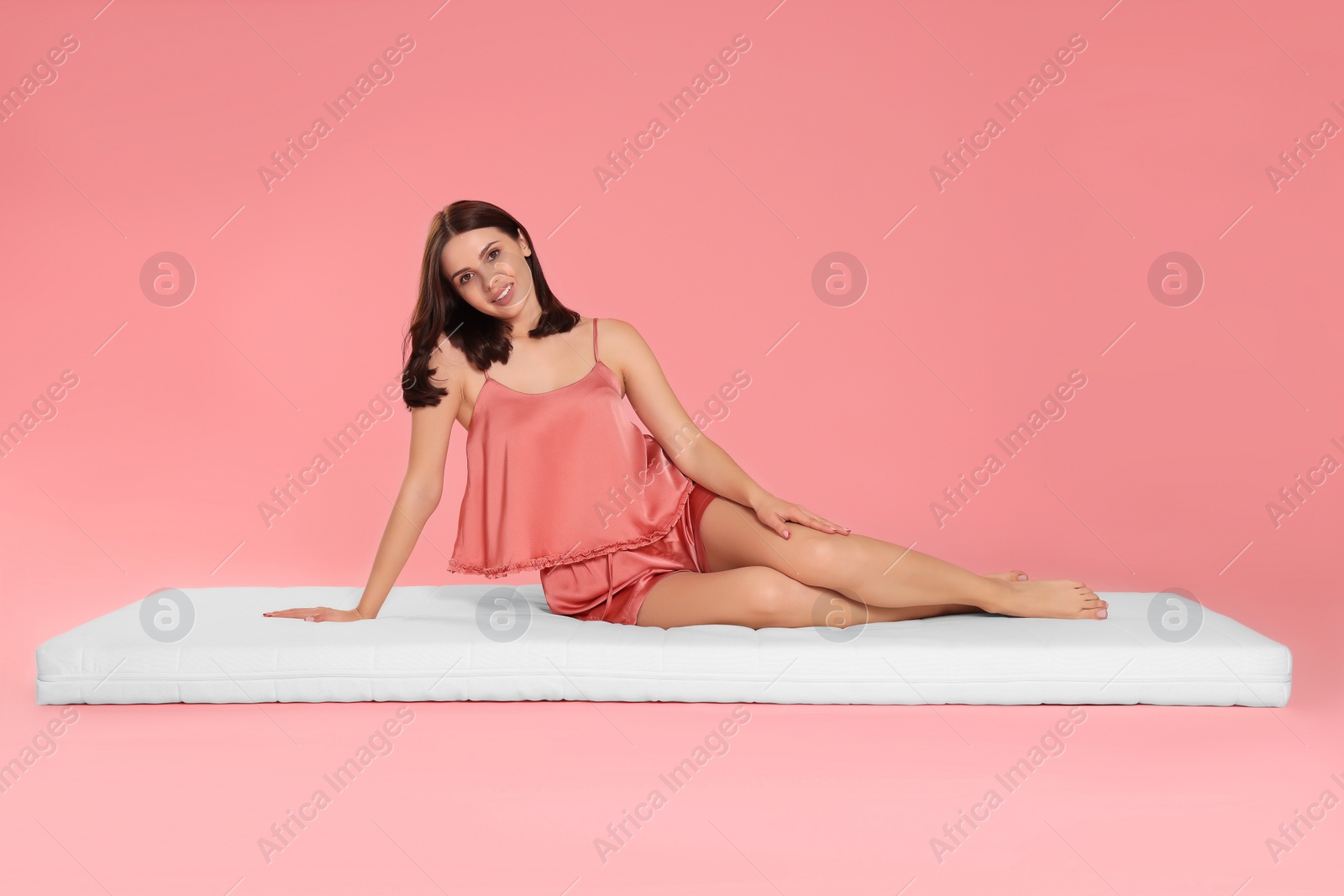 Photo of Young woman sitting on soft mattress against pale pink background