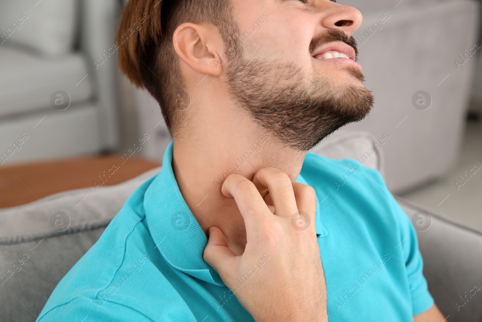 Photo of Young man scratching neck at home, closeup. Annoying itch