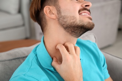Photo of Young man scratching neck at home, closeup. Annoying itch