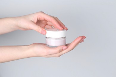 Woman holding jar of cream on grey background, closeup