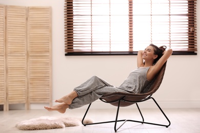 Photo of Young woman relaxing in chair near window with blinds at home. Space for text